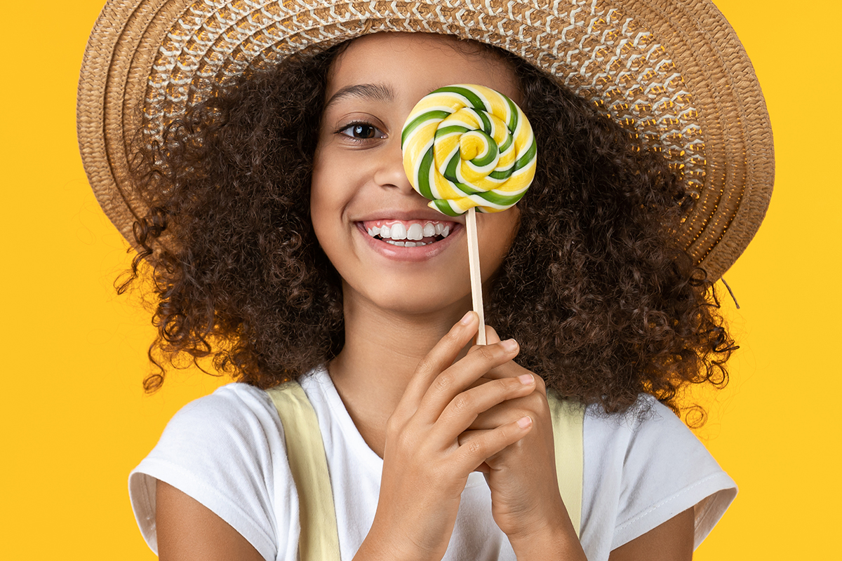 Young African Girl Kid In Hat With Candy Isolated Over Yellow Background