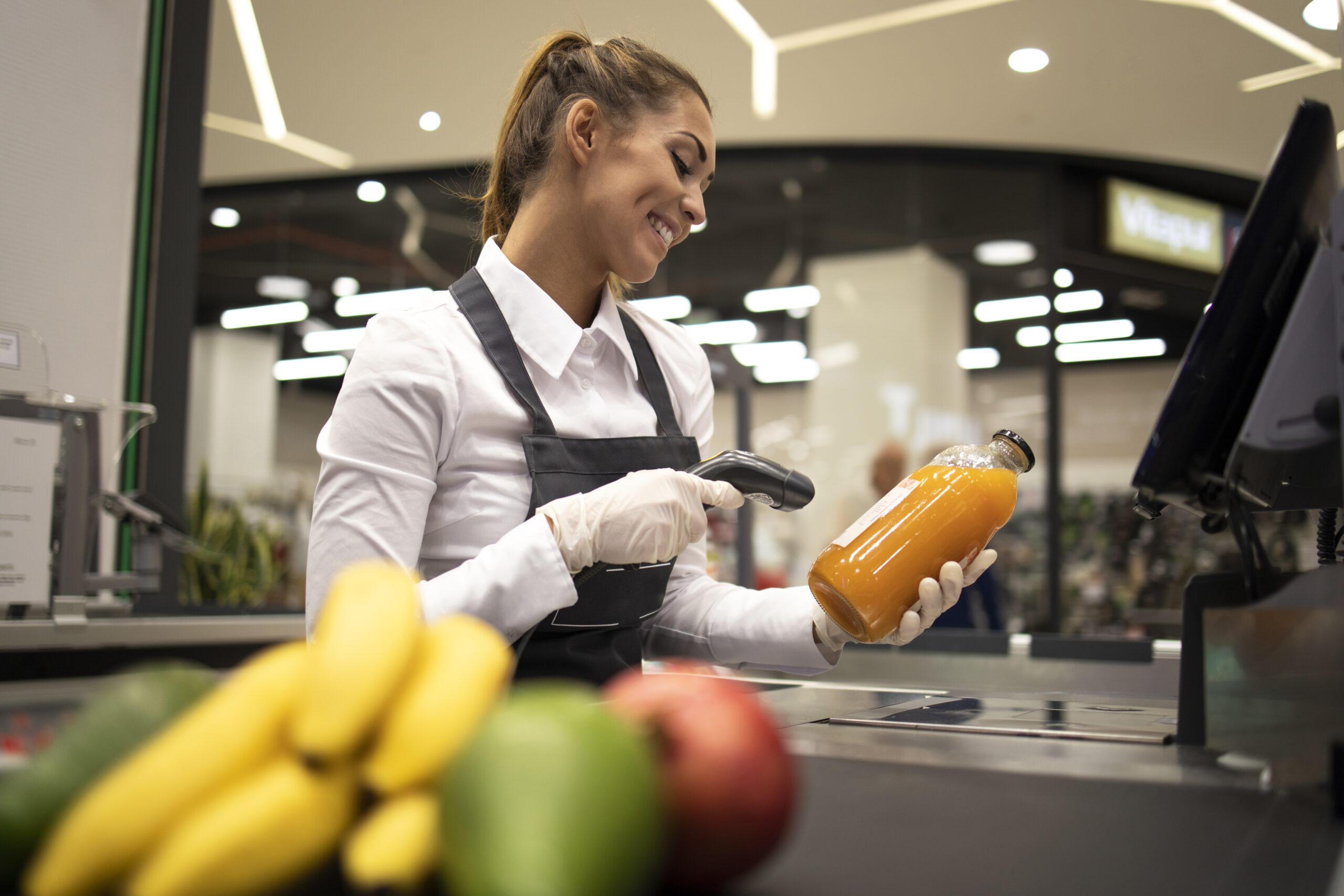 Portrait Of Female Cashier In Supermarket Scanning Bar Code Of Products For Sale.